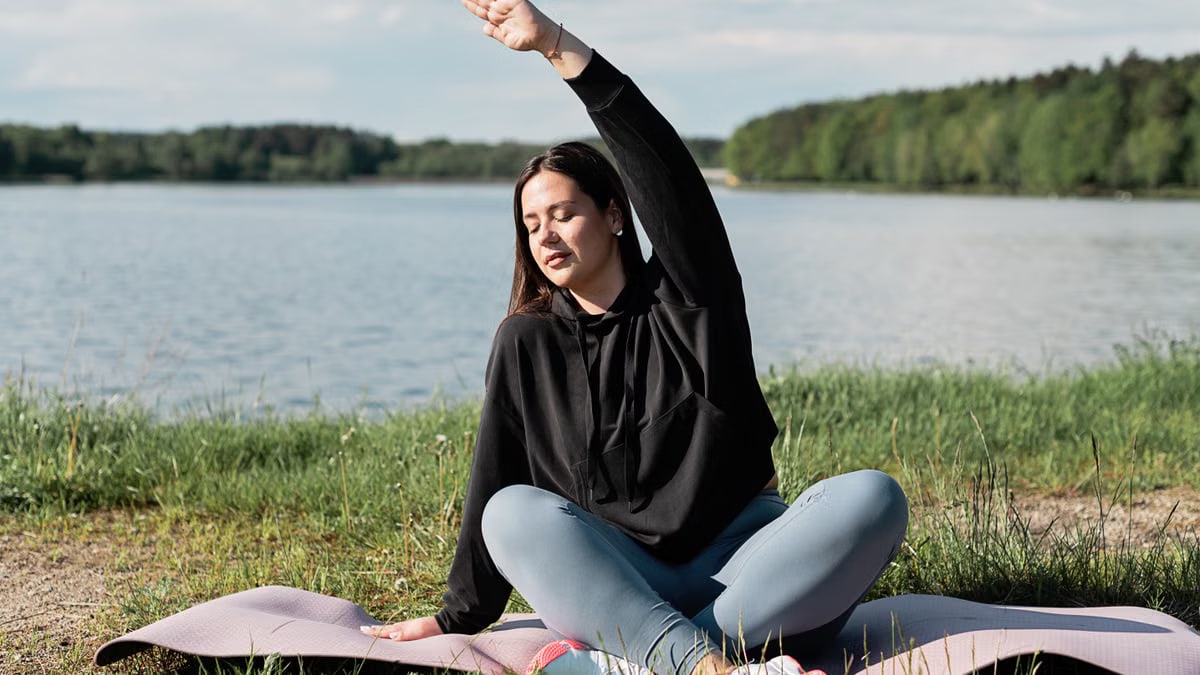 Woman enjoying a relaxing yoga session by a scenic lakeside. Perfect outdoor wellness setting.